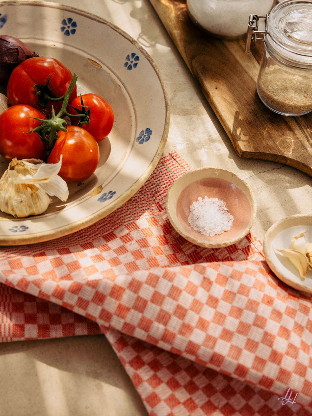 Ein Teller mit Tomaten und Knoblauch, eine Salzschale und ein Glas stehen auf einer Holzfläche mit einem karierten Küchentuch darunter.