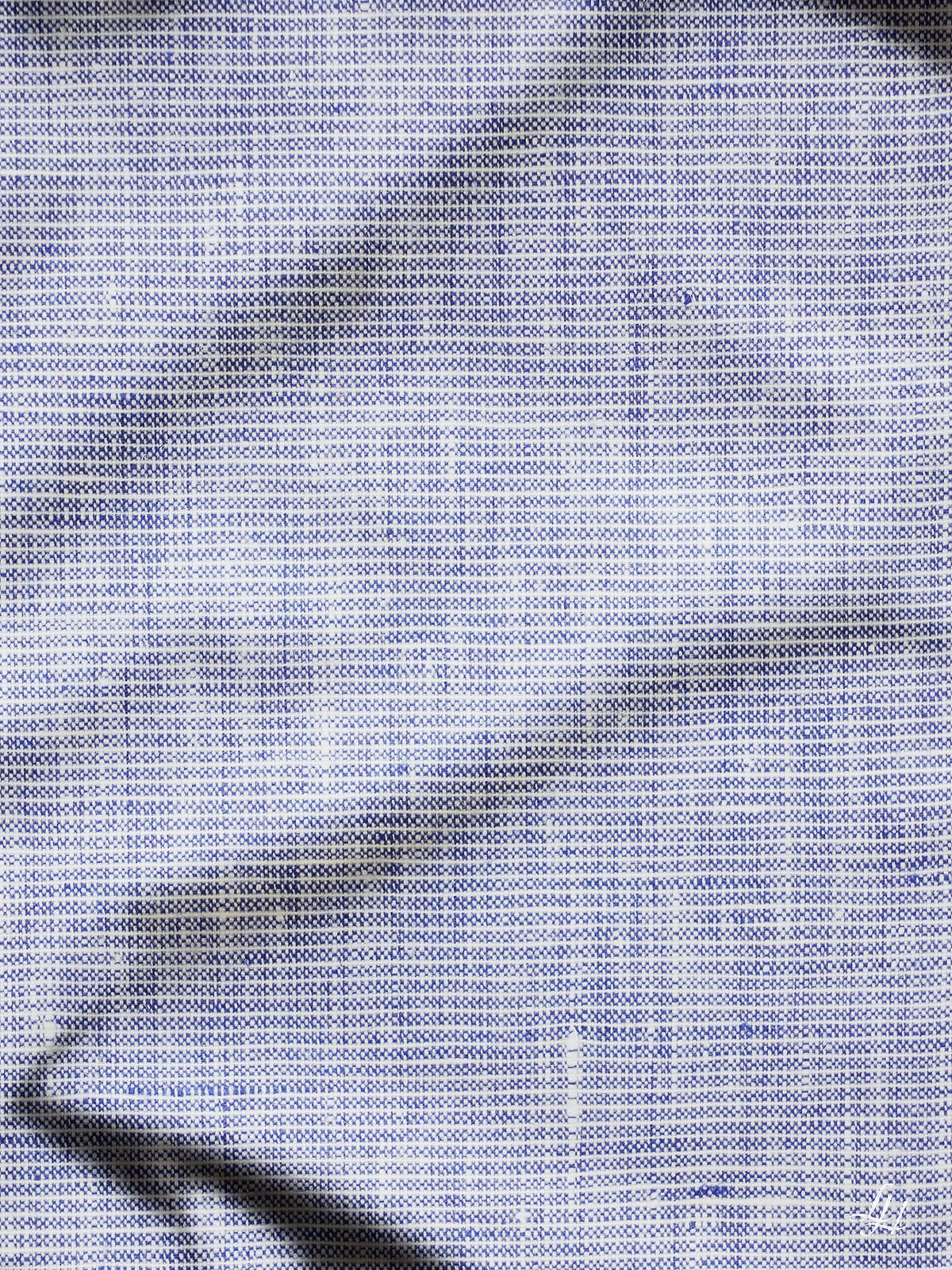 Nahaufnahme eines hellblauen Leinenbettlakens mit schwarzen Falten und einem Muster aus kleinen Punkten auf der strukturierten Oberfläche.