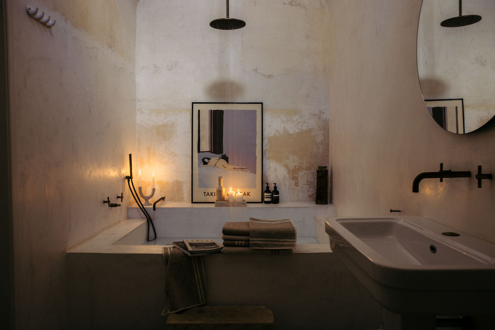 Rustikales Badezimmer mit Badewanne, Regenduschkopf von oben und Waschbecken, Leinenhandtücher am WannenrandKerzen