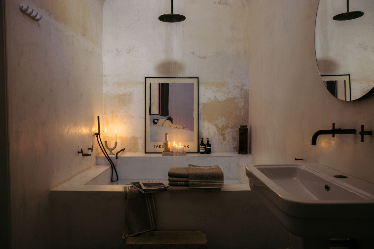 Rustikales Badezimmer mit Badewanne, Regenduschkopf von oben und Waschbecken, Leinenhandtücher am WannenrandKerzen