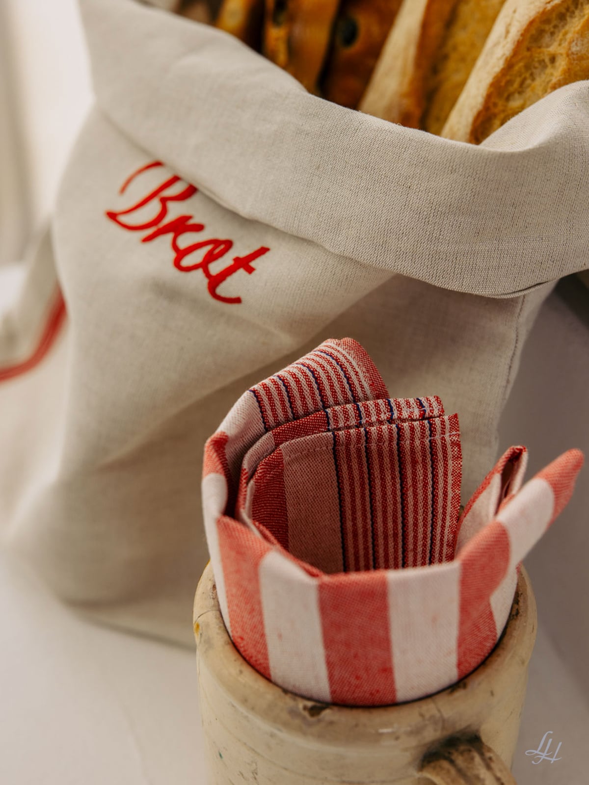 Eine Brotbeutel-Halbleine mit Baguette und rot-gestreiften Servietten in einer Tasse - für natürliche Brotaufbewahrung.