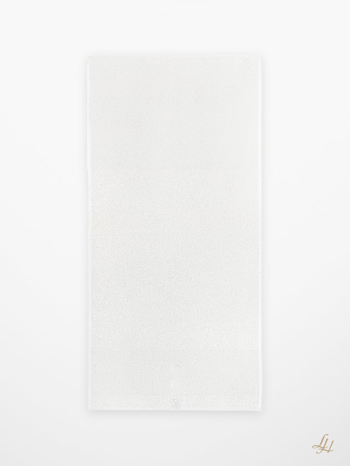 Ein rechteckiges weißes Leinenfrotté Saunatuch liegt flach auf und ist mit einem kleinen goldenen Monogramm in der rechten unteren Ecke versehen.